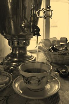 a coffee cup sitting on top of a saucer next to a metal pot filled with liquid