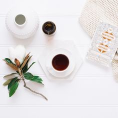 a cup of tea next to some flowers on a white table