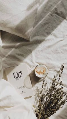 an open book sitting on top of a bed next to a cup and saucer