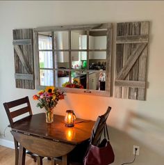 a wooden table with a candle and flowers on it in front of a mirror that has shutters