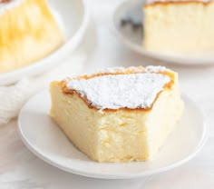 a piece of cake with powdered sugar on top sits on a plate next to another slice