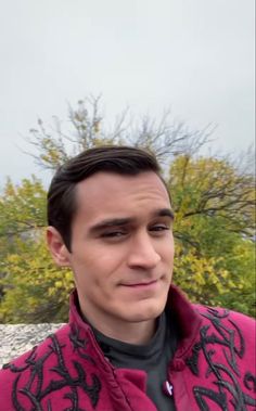 a man wearing a red and black jacket with trees in the background