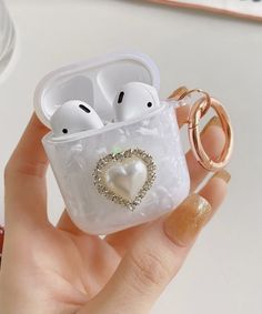 a hand holding an airpods case with two white hearts on it and a gold ring