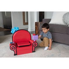 a little boy sitting on the floor next to a red chair