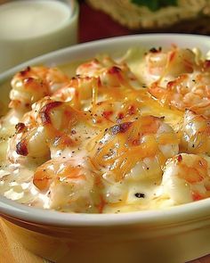 a bowl filled with shrimp and cheese on top of a table next to a glass of milk