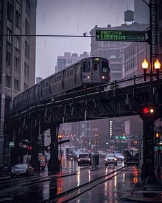 a train is going over a bridge in the city on a rainy day with traffic