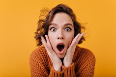 a woman making a surprised face with her hands over her mouth on an orange background