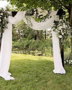 an outdoor wedding ceremony setup with white flowers and draping on the arbors