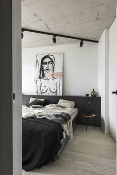 a bedroom with white walls and wood flooring is pictured in this image, there is a large painting on the wall above the bed