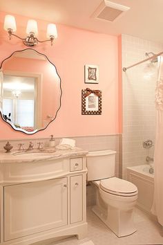 a bathroom with pink walls, white fixtures and an oval mirror above the toilette