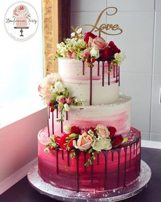 a three tiered cake with flowers and dripping icing on the top is sitting on a table