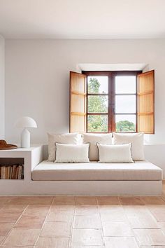 a white couch sitting under a window next to a book shelf