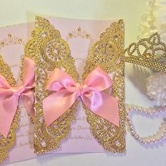 a pink and gold wedding card with a tiara next to it on a table