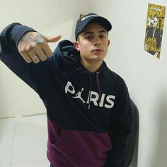 a young man in a black and purple hoodie pointing at the camera with his finger