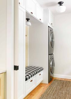 a washer and dryer in a white laundry room with wood flooring, built - in cabinets and drawers