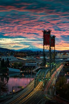 the sun is setting over a city with mountains in the background and cars driving on the road