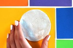 a woman's hand holding a white doughnut on top of colorful squares and rainbows