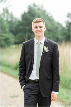 a man in a suit and tie standing on a dirt road with trees in the background