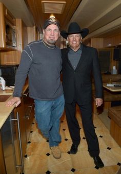 two men in cowboy hats standing next to each other at a kitchen counter with wooden cabinets