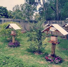 three bird houses in the middle of a grassy area with trees and flowers around them