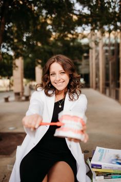 a woman sitting on the ground holding a can and toothbrush in one hand while smiling at the camera