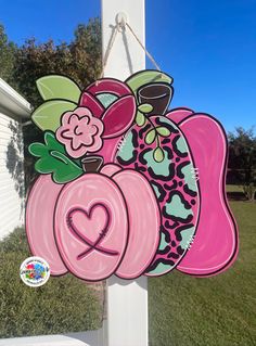 a sign with flowers and hearts hanging from the side of a white pole in front of a house