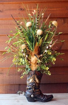 a vase with flowers in it sitting on a table next to a wooden wall and a pair of cowboy boots