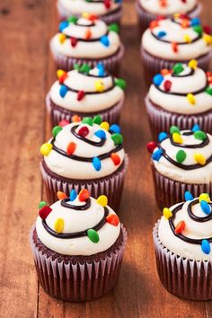 cupcakes with white frosting and colorful sprinkles are arranged on a wooden table