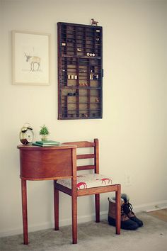 a small wooden desk with a chair next to it in front of a painting on the wall