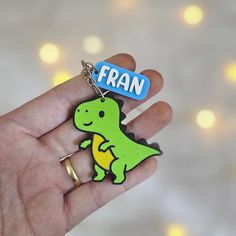 a hand holding a small keychain that says fran with a dinosaur on it