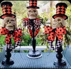 three halloween decorations with skulls wearing top hats and checkered bow ties, sitting on a table in front of a window