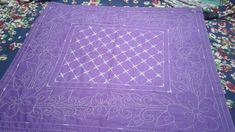 a purple table cloth with white stitching on it sitting on top of a bed