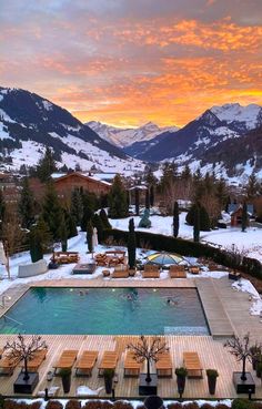 an outdoor swimming pool surrounded by snow covered mountains in the distance, with lounge chairs around it