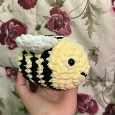 a hand holding a small crocheted toy with a black and white bee on it