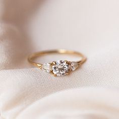 a three stone diamond ring on a white fabric background, with the focus on the engagement ring