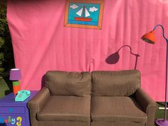 a brown couch sitting in front of a pink wall with a lamp on top of it