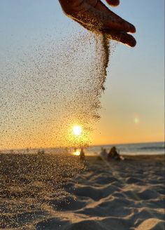 a person is throwing sand into the air on the beach as the sun sets in the background