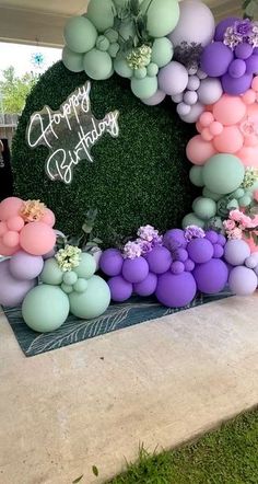 an outdoor birthday party with balloons and flowers on the wall, surrounded by greenery