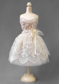 a white dress on a mannequin with lace and flowers in the skirt,