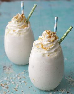 two glasses filled with whipped cream on top of a blue table next to a carton of almond milk