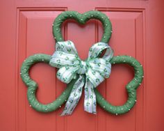 a shamrock shaped wreath hanging on a red door with a green bow and white ribbon