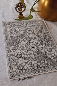 a white table cloth with an owl and flowers on it next to a gold vase