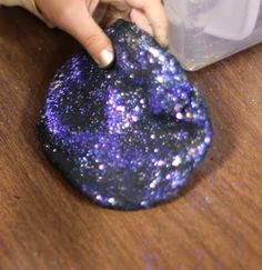 a hand touching a purple and black object on top of a wooden table next to a rock