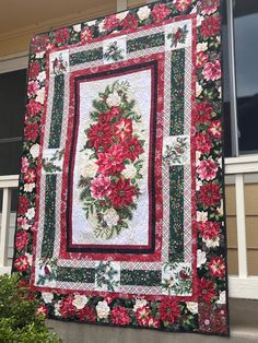 a red and white quilt hanging from the side of a building with flowers on it