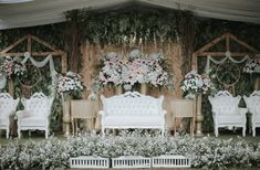 an elaborately decorated stage set up with white furniture and floral arrangements on the wall