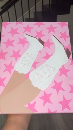 a hand holding up a pink and white painting with stars on it's sides