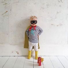 a little boy dressed up as a clown standing in front of a white wall wearing a mask and yellow rubber boots