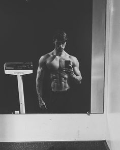 a shirtless man taking a selfie in front of a mirror with his cell phone