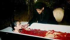 two people in a bathtub with rose petals on the floor and one person touching her face