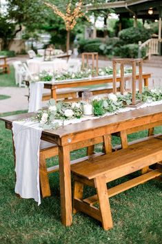 a wooden table with white flowers and greenery is set up for an outdoor dinner